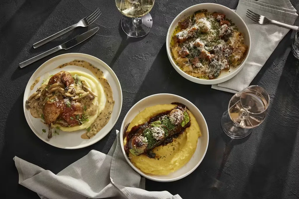 Three gourmet dishes, wine, and silverware, seen from above.
