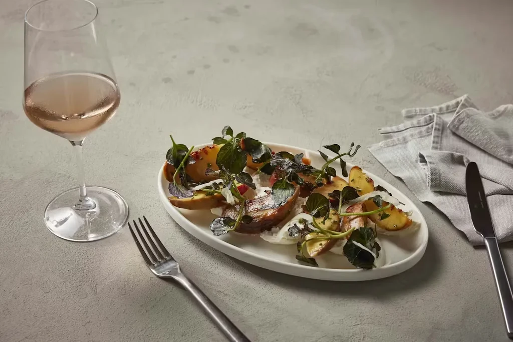 Plated appetizer with roasted potatoes, greens, sauce, and chilled rosé wine.