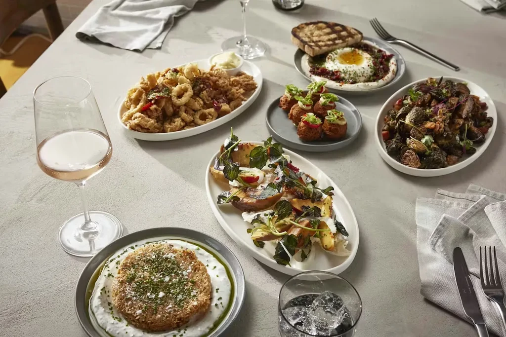 Assorted restaurant dishes and drinks, including calamari and salad, on a grey table.
