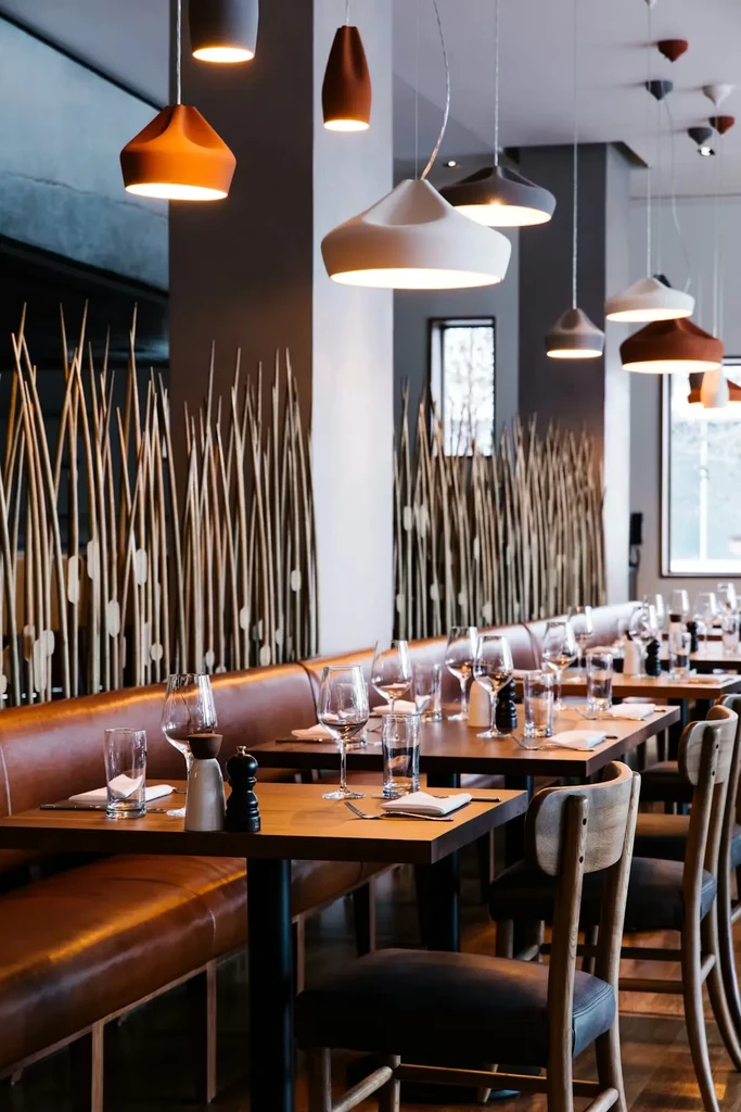Modern restaurant interior with banquette seating, set tables, and wooden screen.