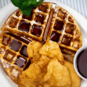 Golden waffle and fried chicken with syrup, powdered sugar, and mint.
