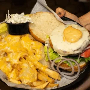 Top-down: Open-faced burger, fried egg, cheese fries, coleslaw, and pickle.