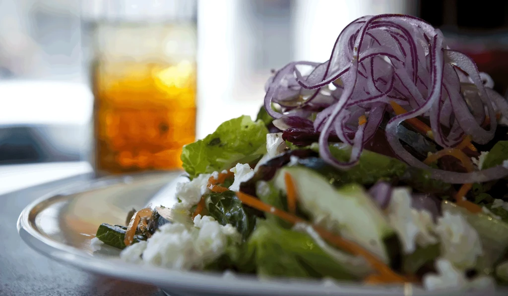 Close-up of vibrant salad with onions, lettuce, cheese, carrots, and iced drink.