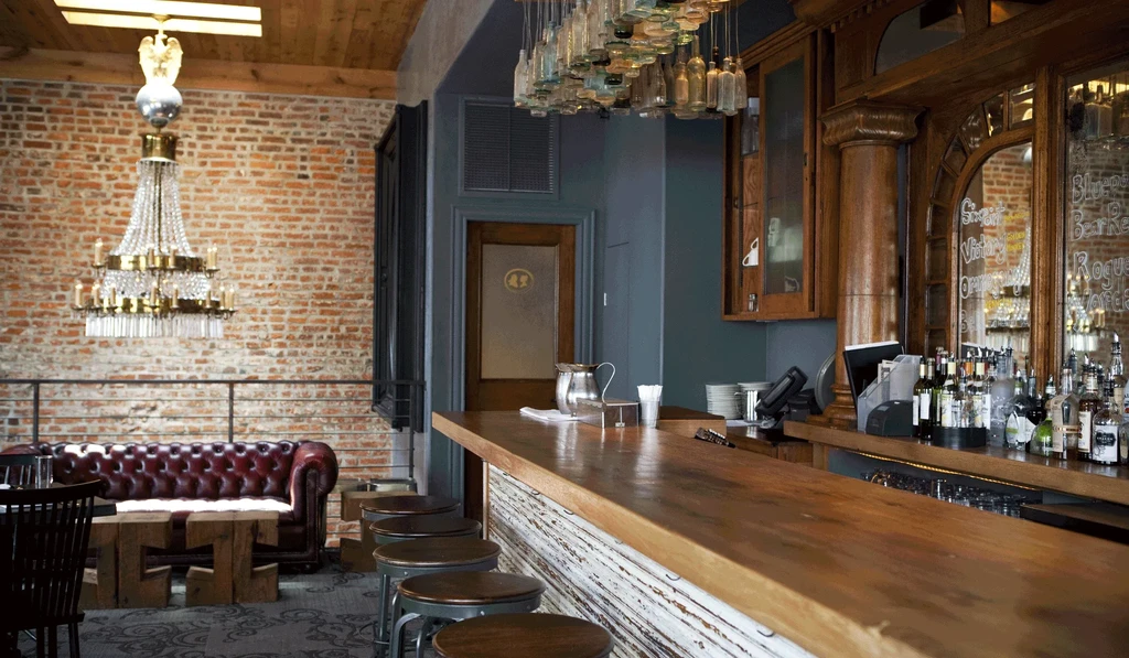 Empty, elegant bar with brick wall, Chesterfield sofa, and wooden counter.