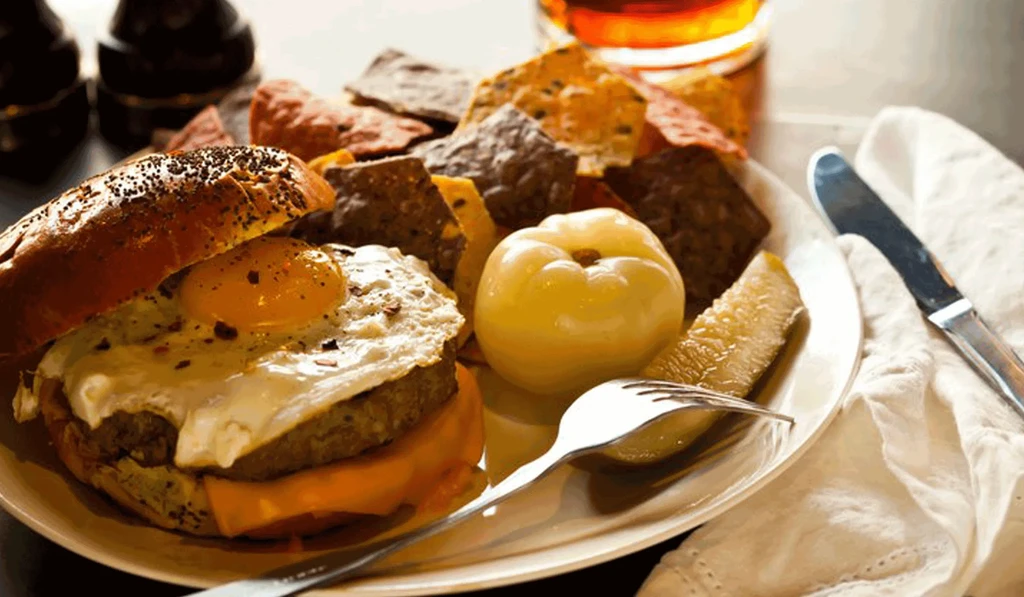 Burger topped with fried egg, melted cheese, chips, and pickle.
