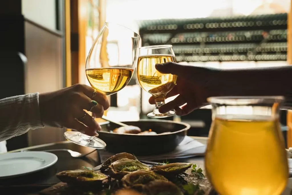 Hands clinking golden drinks, green ring prominent, above oysters.