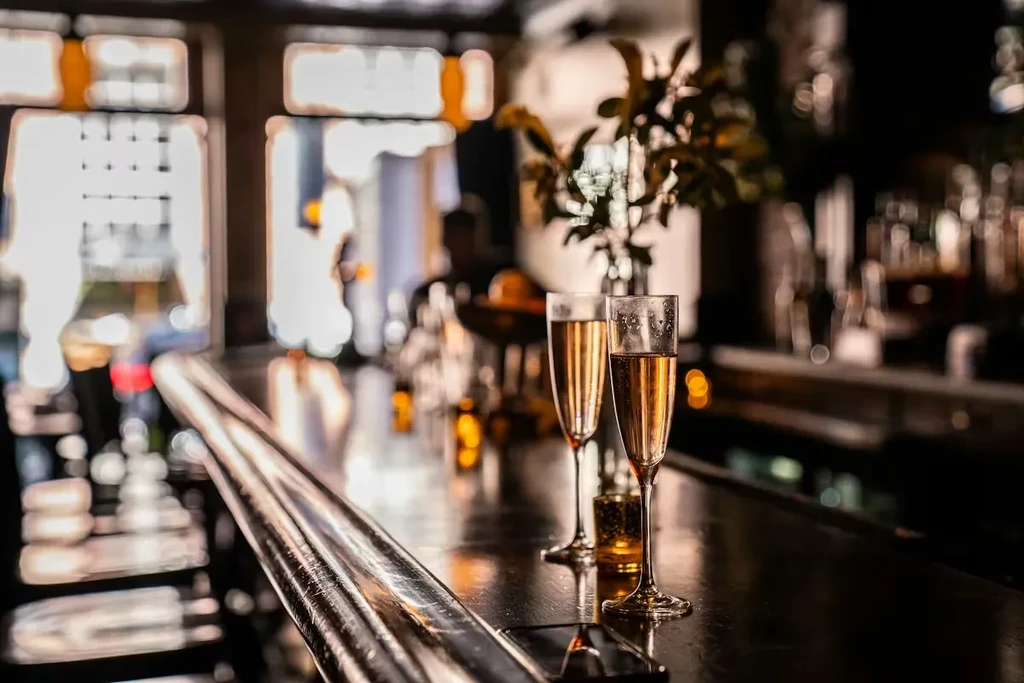 Two champagne flutes with condensation on a dark, reflective bar.