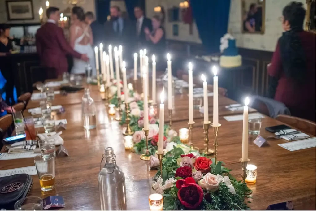 Elegant wooden table with lush roses, lit candles, and blurred guests.