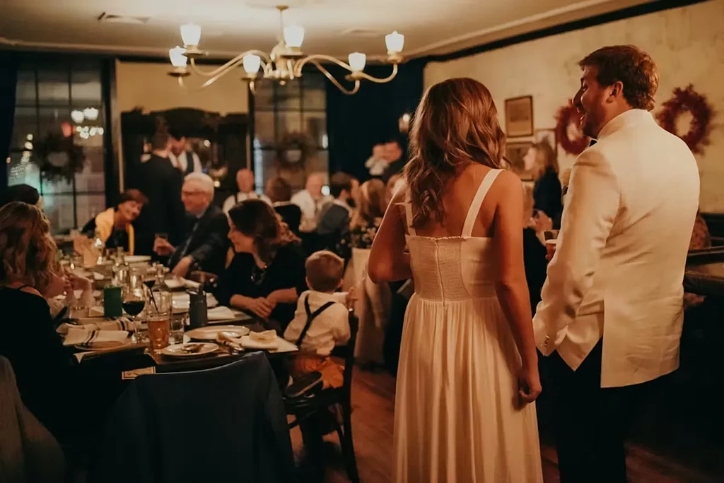 Smiling couple in white at a warmly lit restaurant reception.