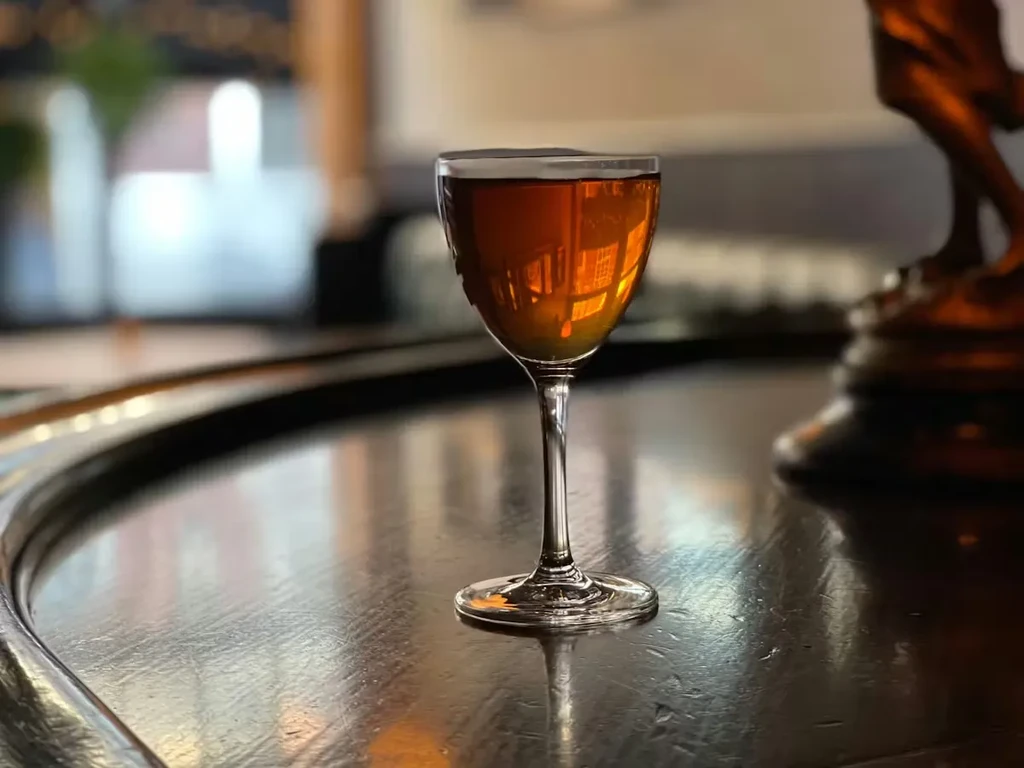 Cocktail glass with amber liquid on a dark wooden surface.
