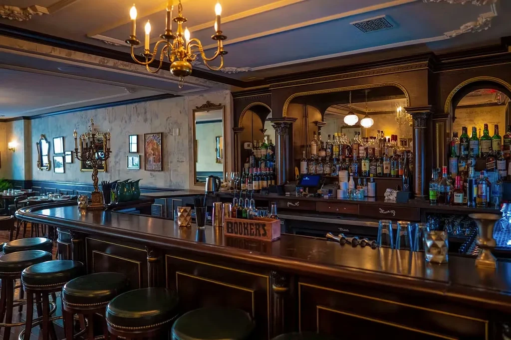 Dark wood bar, green stools, well-stocked liquor shelves, warm lighting.