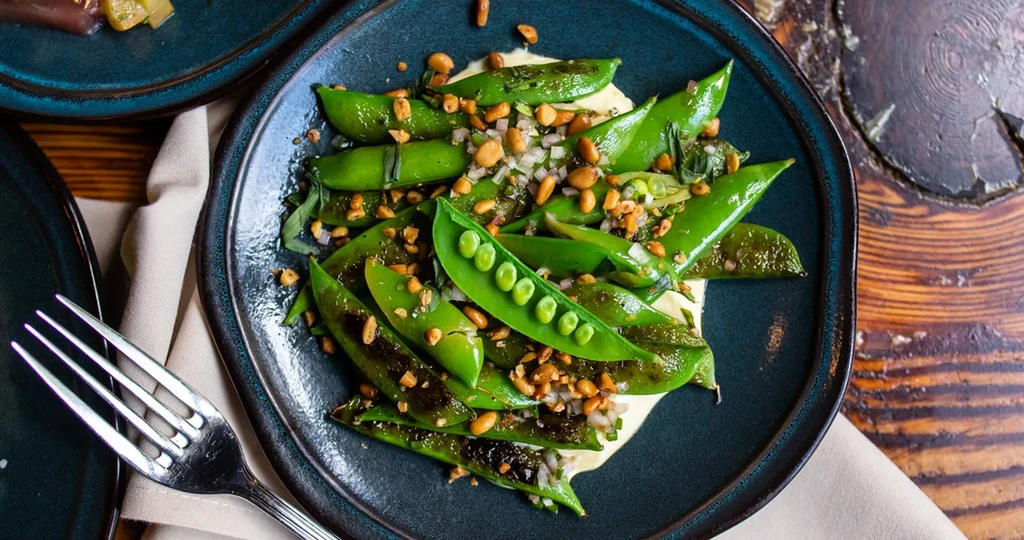 Vibrant snap peas plated with sauce and garnishes on a blue plate.