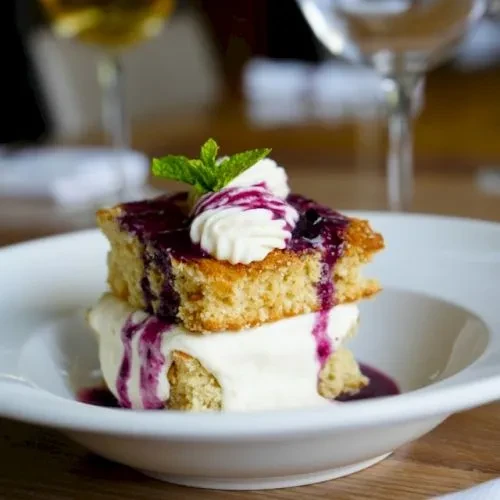 Plated square cake, berry compote, whipped cream, mint, and ice cream.