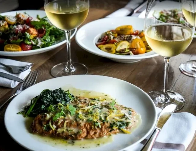 Warmly lit dining table with fish, salad, colorful vegetables, and wine.