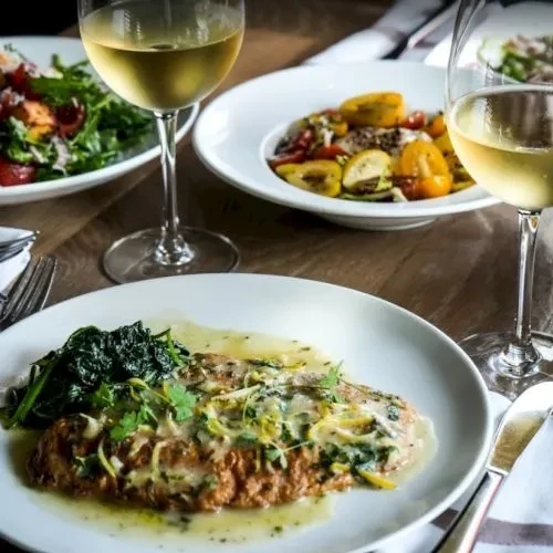 Restaurant table with pan-seared fish, leafy greens, wine, and salad.