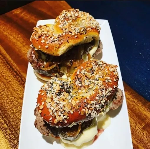 Two mini-burgers with caramelized onions, cheese, and everything pretzel buns.