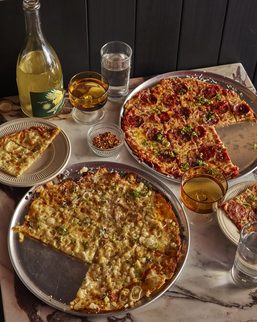 Overhead shot of a marble table with two pizzas and drinks.