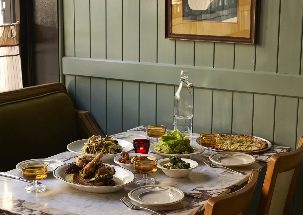 Restaurant table with roasted chicken, pasta, salad, pizza, and drinks.