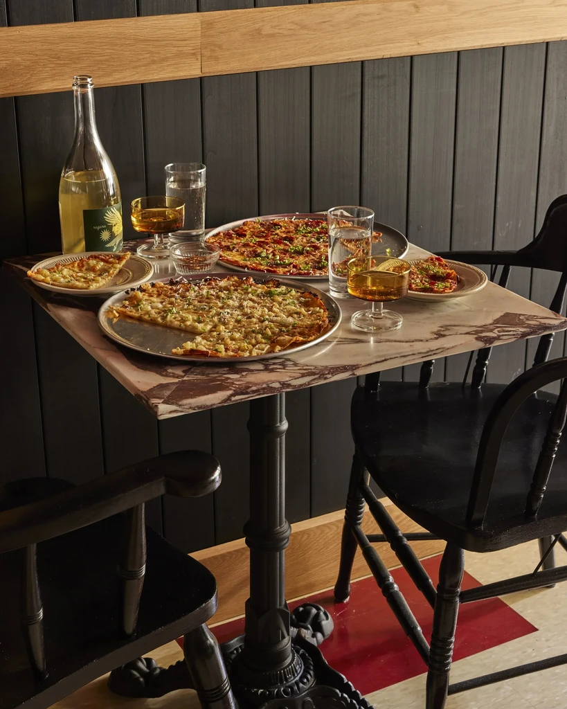 Two pizzas, drinks, and chairs on a marble restaurant table.