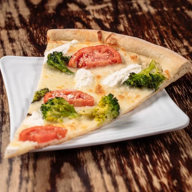 Triangular white pizza slice with broccoli, tomato, and ricotta.