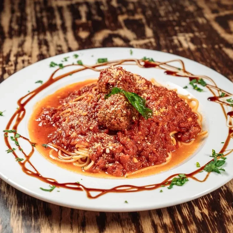 Close-up of spaghetti and meatballs with tomato sauce, Parmesan, and basil.