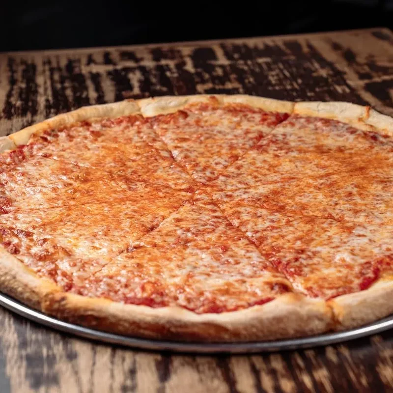Sliced round cheese pizza on silver pan, rustic wood table.