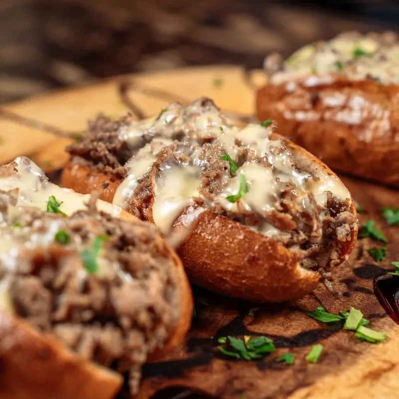 Multiple meat subs topped with melted cheese and fresh herbs.
