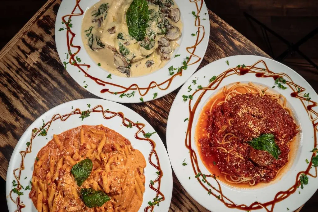 Three pasta dishes: creamy, penne, and spaghetti, on dark wood.