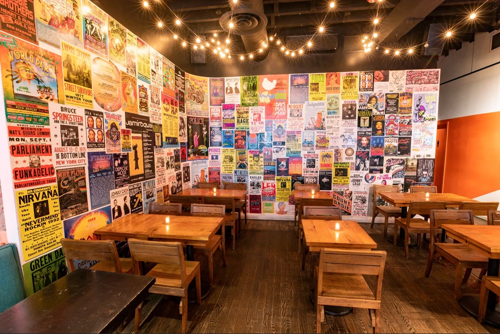 Restaurant dining area with wooden tables and vintage concert posters.