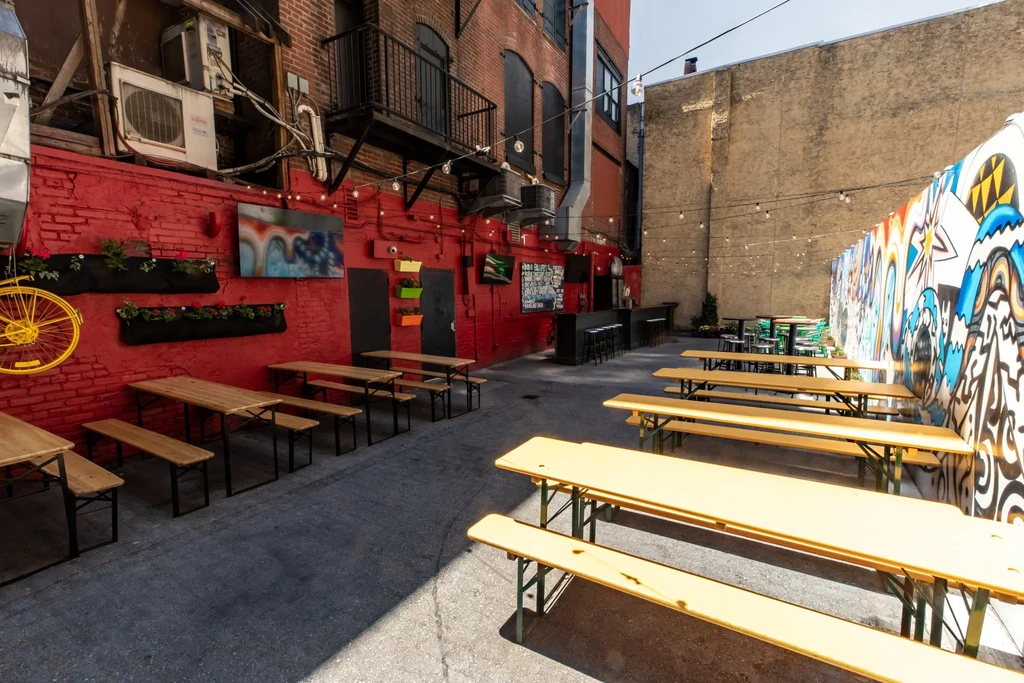 Empty outdoor restaurant patio with picnic tables, string lights, and graffiti mural.