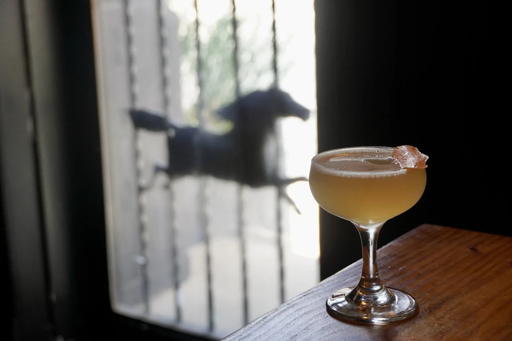 Pale yellow cocktail with curly garnish on wood, blurred animal background.