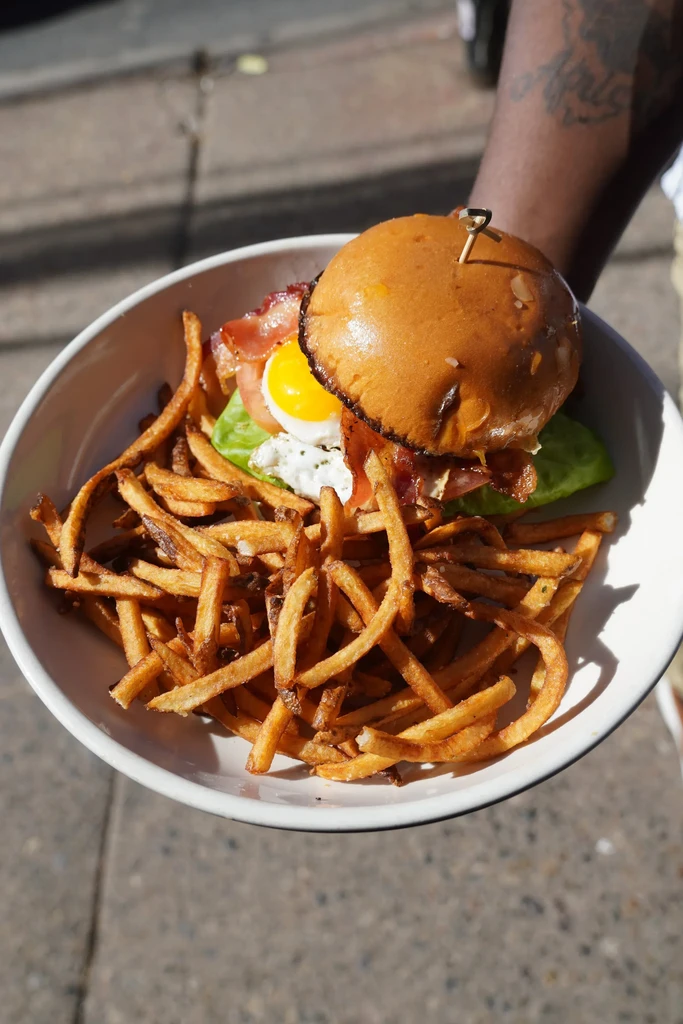 Person holding burger with fried egg and golden fries.