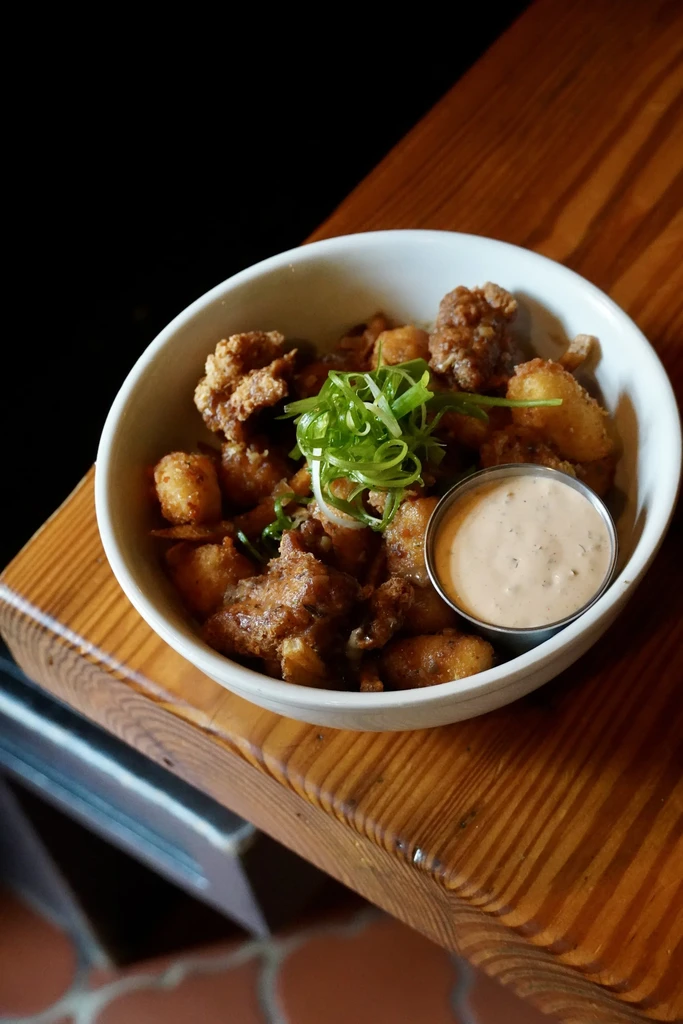 White bowl of fried chicken, cheese curds, green onions, and dipping sauce.