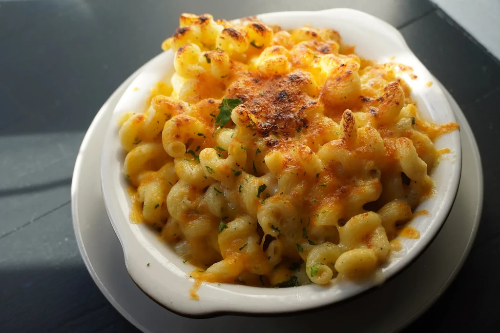 Baked mac and cheese in white bowl with herbs on dark surface.