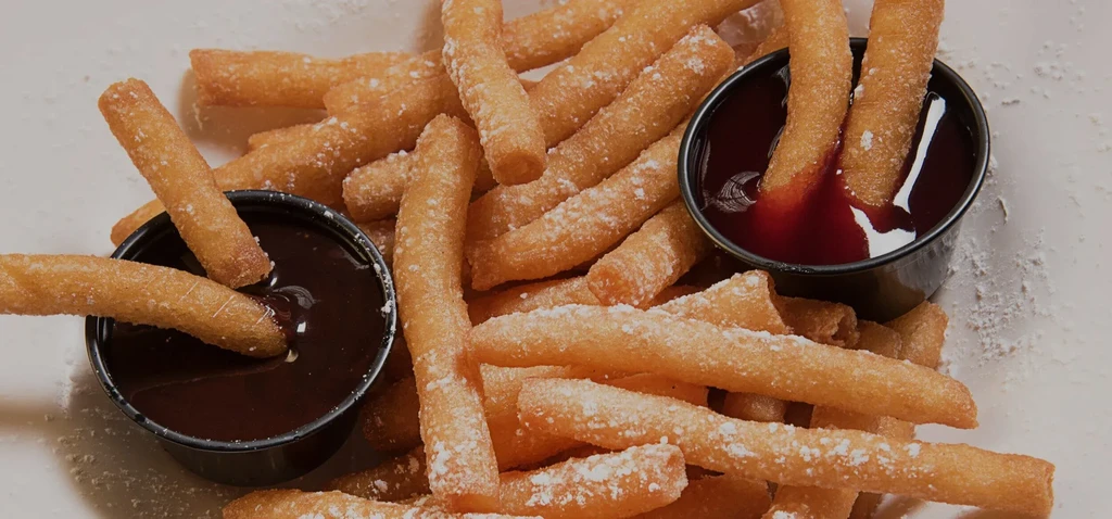 Golden-brown churros dusted with sugar, dipped in chocolate and strawberry sauces.