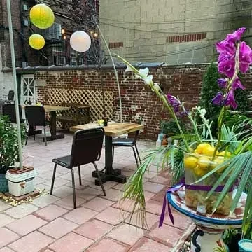 Bright outdoor dining patio with tables, purple flowers, lemons, and lanterns.