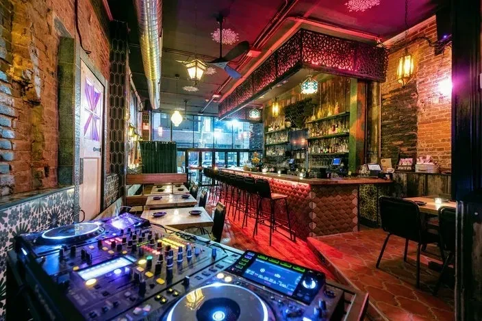 Vibrant restaurant interior with DJ setup, bar, and colorful lighting.