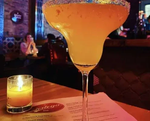 Large orange margarita with salted rim, candle, and Bodega Bar menu.