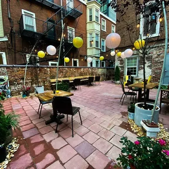 Paved outdoor patio with wooden tables, string lights, plants, and art.