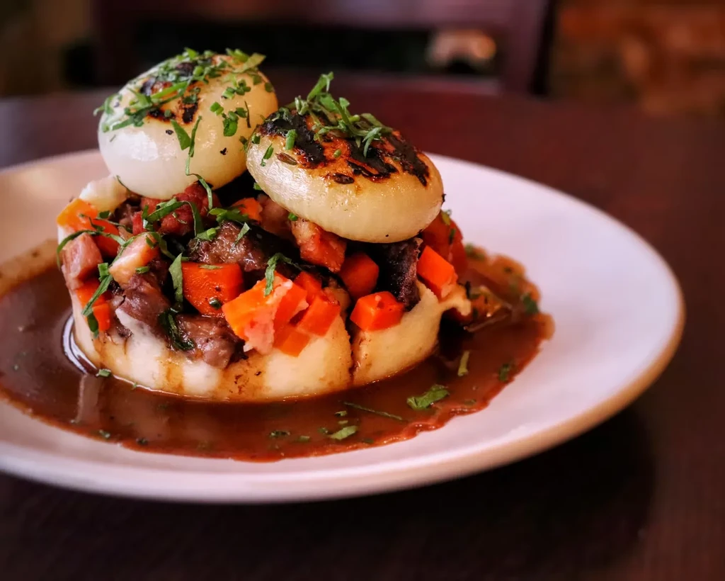 Braised meat with carrots, pearl onions, mashed potatoes, and gravy.