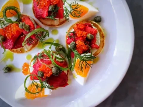 Overhead: Blinis, cured salmon, orange caviar, egg, green garnishes.