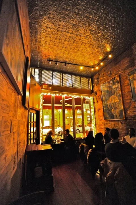 Warmly lit restaurant interior with ornate ceiling, exposed brick, and patrons.