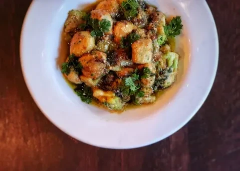 Close-up of golden gnocchi with green vegetables, savory sauce, and fresh herbs.