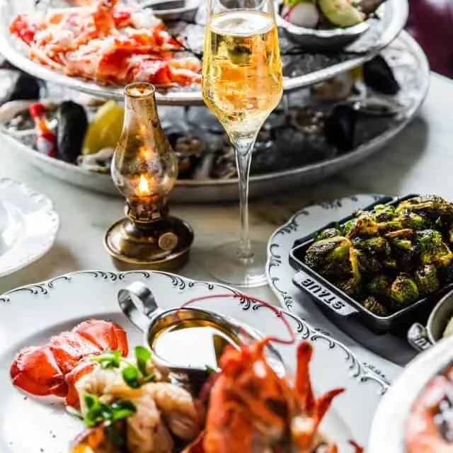 Elegant dining table with lobster, brussels sprouts, seafood tower, and champagne.