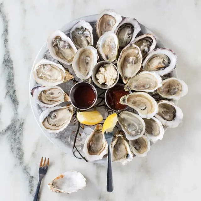 Fresh shucked oysters on ice with lemon, sauces, and oyster forks.