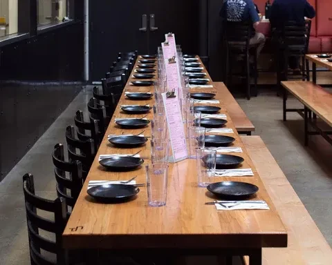 Restaurant's long communal table set with plates, glasses, chopsticks, and menus.