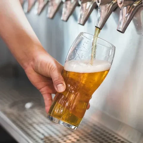 Golden beer fills a glass from a tap, held by hand.