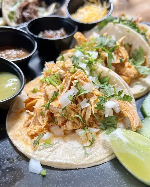 Close-up: Shredded chicken tacos with onions, cilantro, salsas, lime, cheese.