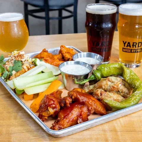Tray of chicken wings, vegetables, and beers on a wooden table.