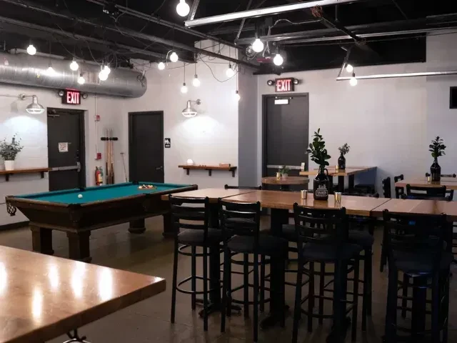 Industrial-chic restaurant interior, wooden tables, pool table, exposed ducts.